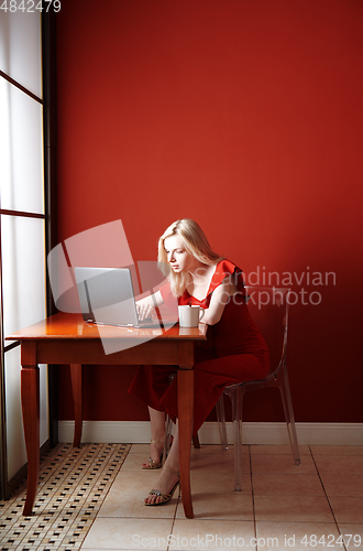 Image of Young adult woman sitting at the table and working on laptop