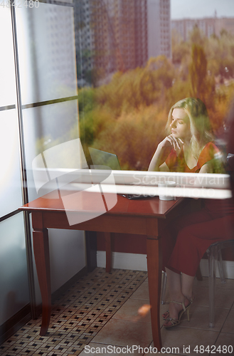 Image of Young adult woman sitting at the table and working on laptop