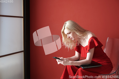 Image of Young adult woman using smartphone and holding laptop