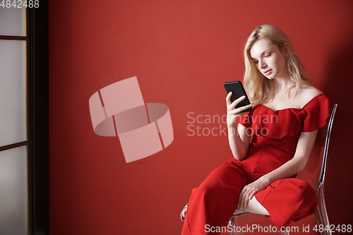 Image of Young adult woman relaxing on a chair and using smartphone