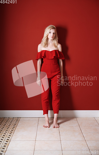 Image of Beautiful young adult woman wearing red jumpsuit standing next t