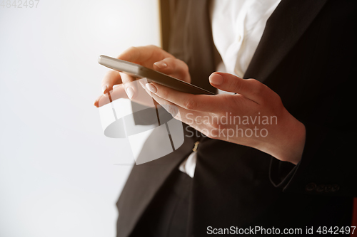 Image of Young adult woman using smartphone next to the white wall