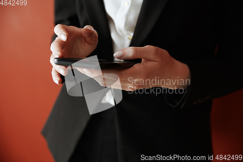 Image of Young adult woman using smartphone next to the red wall