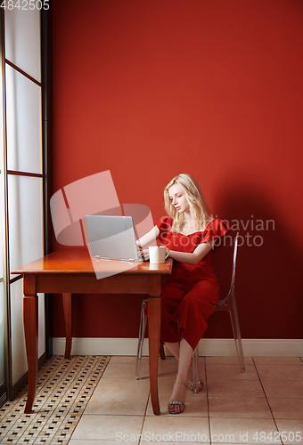 Image of Young adult woman sitting at the table and working on laptop