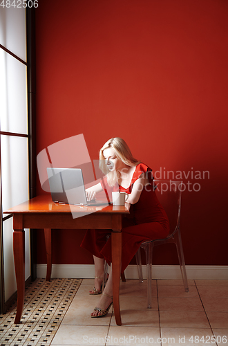 Image of Young adult woman sitting at the table and working on laptop