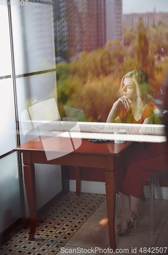 Image of Young adult woman sitting at the table and working on laptop