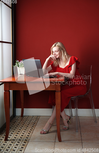 Image of Young adult woman sitting at the table and working on laptop