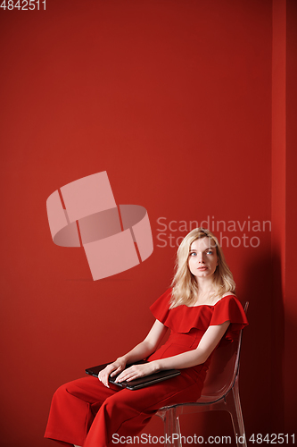 Image of Young adult woman sitting on a chair and holding laptop