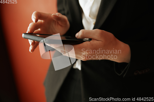 Image of Young adult woman using smartphone next to the red wall