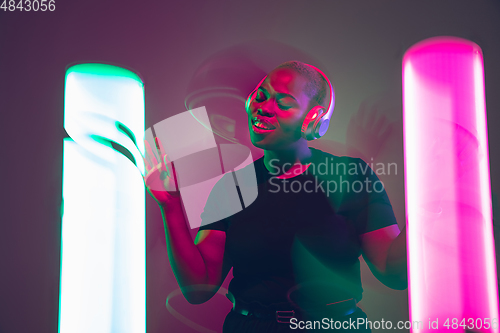 Image of African-american young woman\'s portrait in headphone and bright neon lights