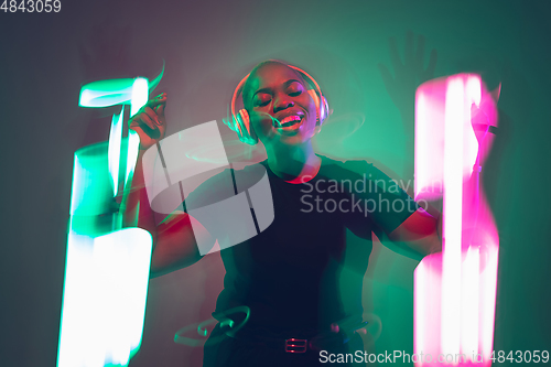 Image of African-american young woman\'s portrait in headphone and bright neon lights