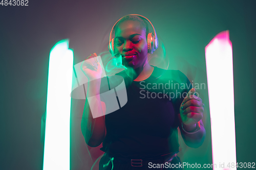 Image of African-american young woman\'s portrait in headphone and bright neon lights