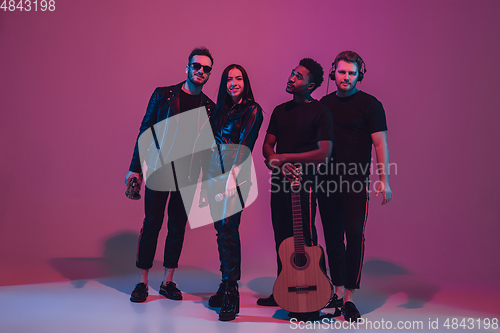 Image of Group of young multiethnic musicians created band, dancing in neon light on pink background