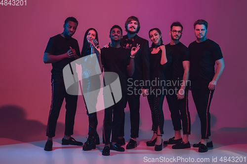 Image of Group of young multiethnic musicians created band, dancing in neon light on pink background