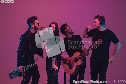 Image of Group of young multiethnic musicians created band, dancing in neon light on pink background