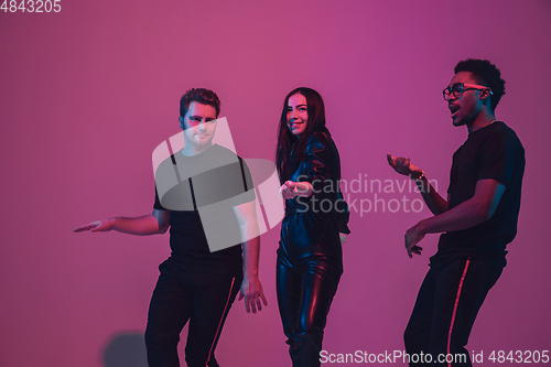 Image of Group of young multiethnic musicians created band, dancing in neon light on pink background