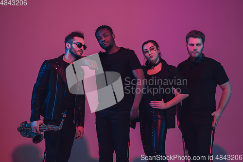 Image of Group of young multiethnic musicians created band, dancing in neon light on pink background