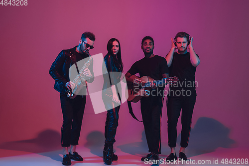 Image of Group of young multiethnic musicians created band, dancing in neon light on pink background