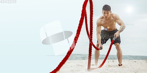 Image of Young healthy man athlete doing exercise at the beach with ropes, flyer with copyspace