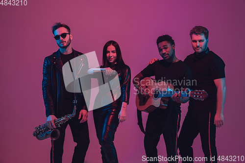 Image of Group of young multiethnic musicians created band, dancing in neon light on pink background