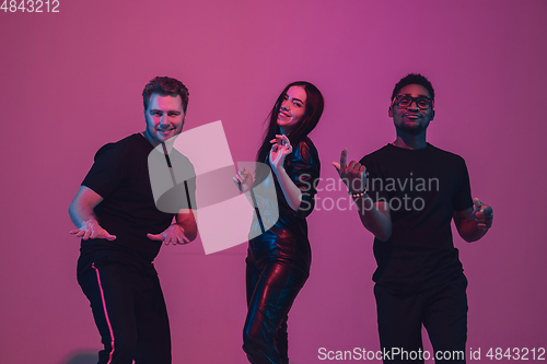 Image of Group of young multiethnic musicians created band, dancing in neon light on pink background