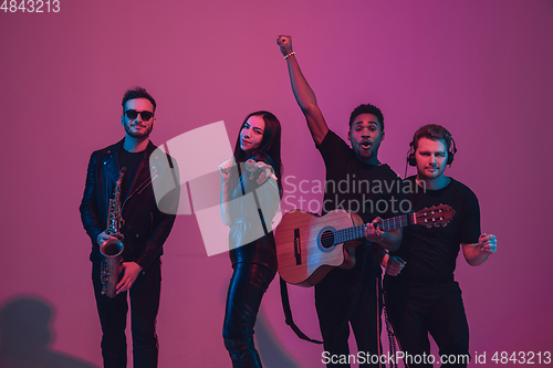 Image of Group of young multiethnic musicians created band, dancing in neon light on pink background