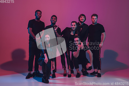 Image of Group of young multiethnic musicians created band, dancing in neon light on pink background