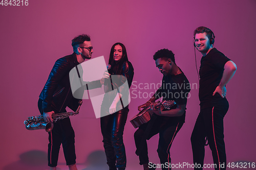 Image of Group of young multiethnic musicians created band, dancing in neon light on pink background