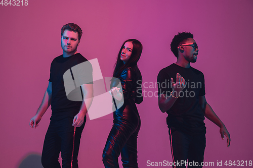 Image of Group of young multiethnic musicians created band, dancing in neon light on pink background