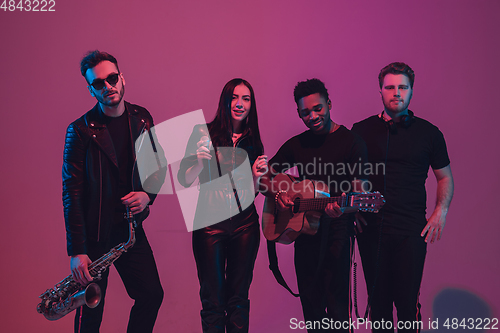 Image of Group of young multiethnic musicians created band, dancing in neon light on pink background