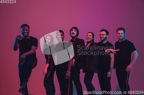 Image of Group of young multiethnic musicians created band, dancing in neon light on pink background