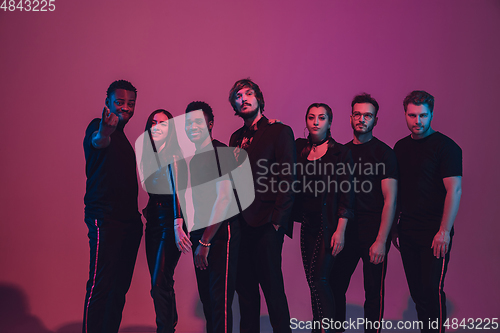 Image of Group of young multiethnic musicians created band, dancing in neon light on pink background