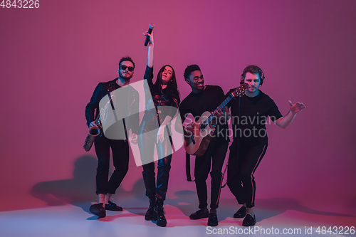 Image of Group of young multiethnic musicians created band, dancing in neon light on pink background