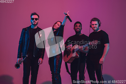 Image of Group of young multiethnic musicians created band, dancing in neon light on pink background