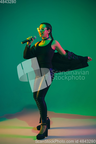 Image of Caucasian female singer portrait isolated on green studio background in neon light