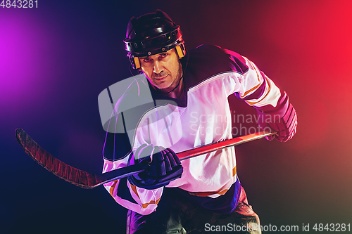 Image of Male hockey player with the stick on ice court and dark neon colored background