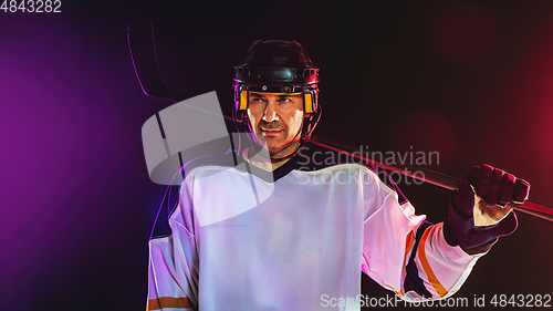 Image of Male hockey player with the stick on ice court and dark neon colored background