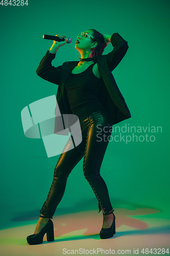 Image of Caucasian female singer portrait isolated on green studio background in neon light