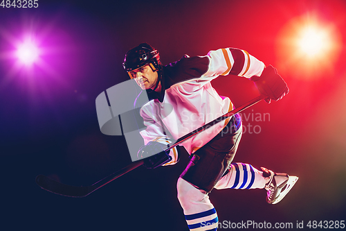 Image of Male hockey player with the stick on ice court and dark neon colored background