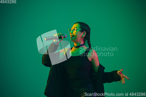 Image of Caucasian female singer portrait isolated on green studio background in neon light