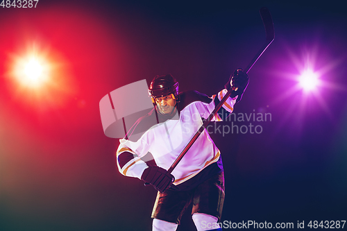 Image of Male hockey player with the stick on ice court and dark neon colored background