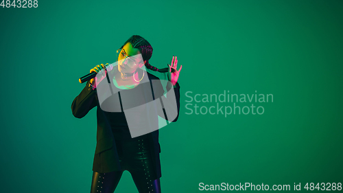 Image of Caucasian female singer portrait isolated on green studio background in neon light