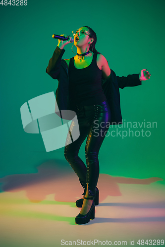 Image of Caucasian female singer portrait isolated on green studio background in neon light