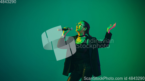 Image of Caucasian female singer portrait isolated on green studio background in neon light