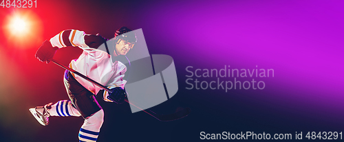 Image of Male hockey player with the stick on ice court and dark neon colored background