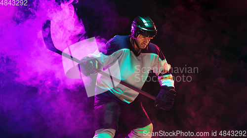 Image of Male hockey player with the stick on ice court and dark neon colored background