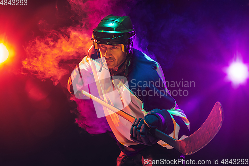 Image of Male hockey player with the stick on ice court and dark neon colored background