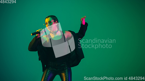 Image of Caucasian female singer portrait isolated on green studio background in neon light