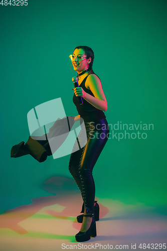 Image of Caucasian female singer portrait isolated on green studio background in neon light