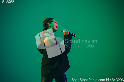 Image of Caucasian female singer portrait isolated on green studio background in neon light